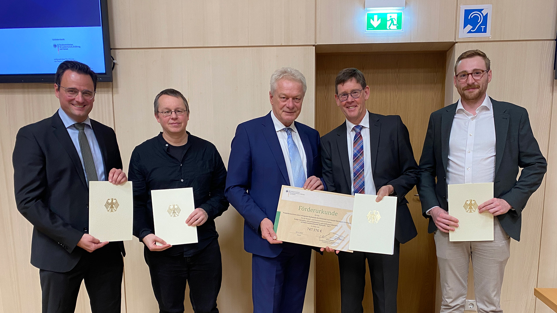Five men standing in front of a wooden wall, each presenting a certificate.