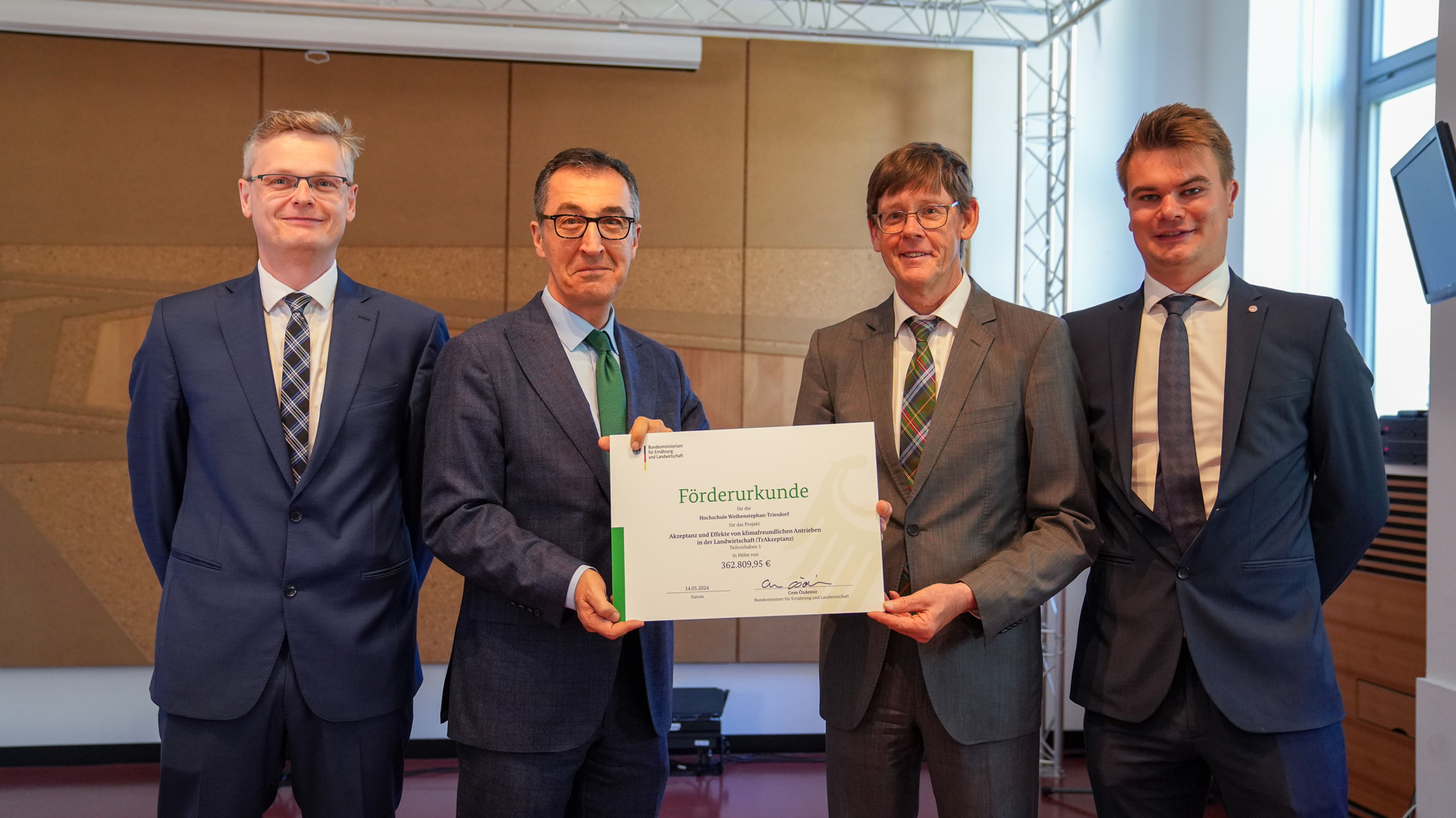 Four men in suits present a symbolic certificate.